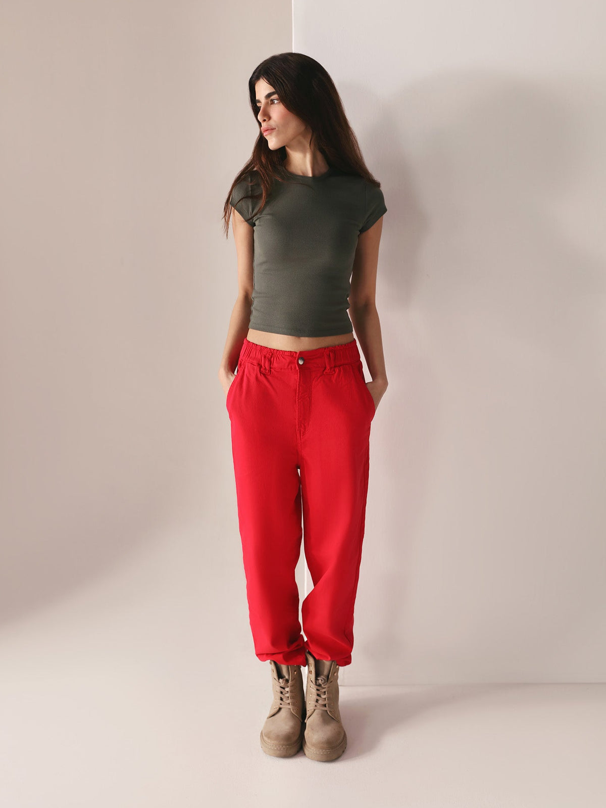 Woman wearing a grey top and casual wear red paper bag pants against a plain background