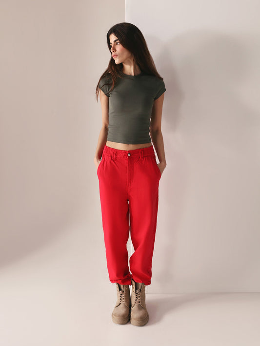 Woman wearing a grey top and casual wear red paper bag pants against a plain background
