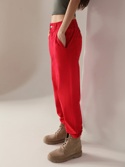 Woman wearing a grey top and casual wear red paper bag pants against a plain background