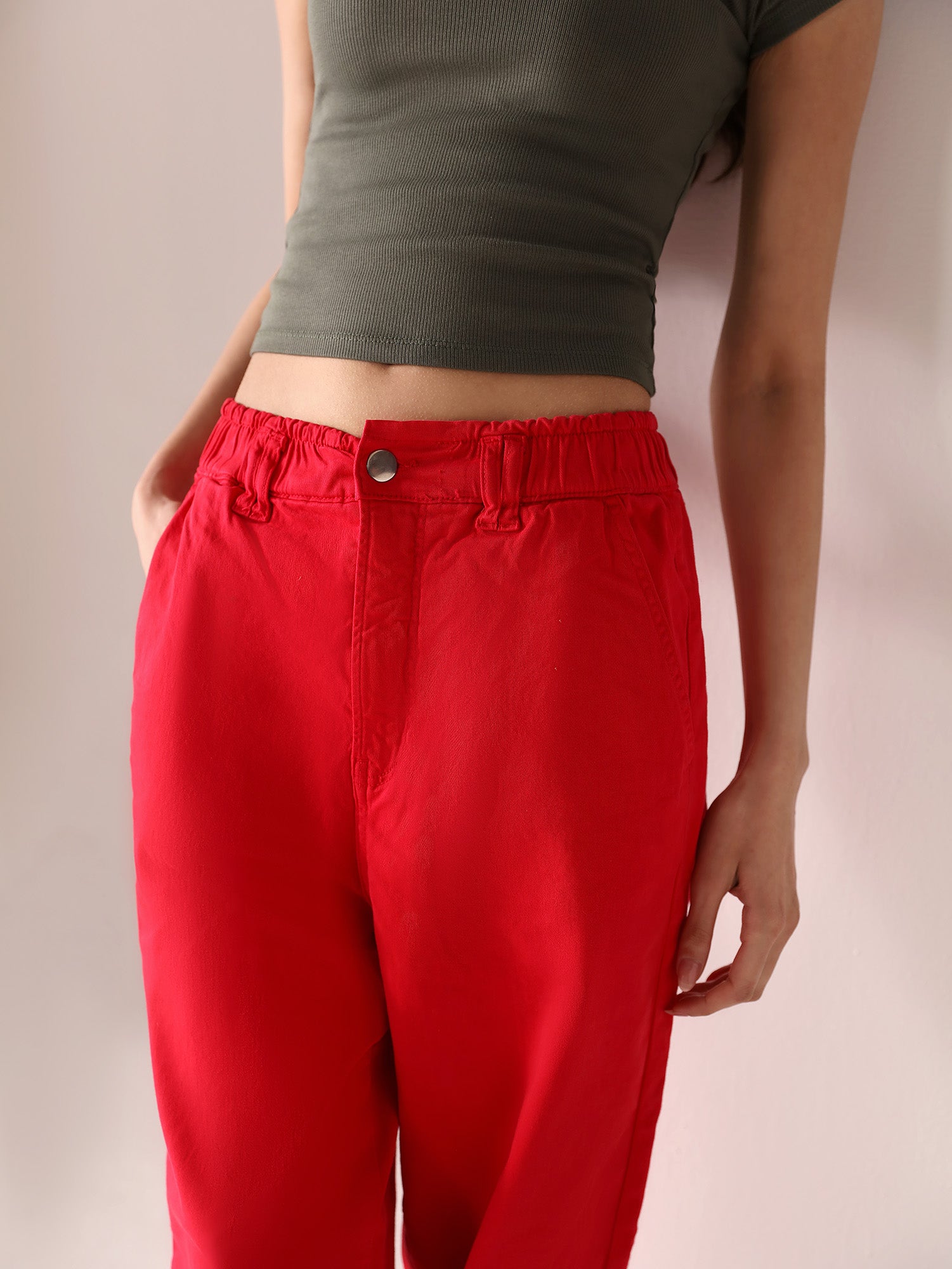 Woman wearing a grey top and casual wear red paper bag pants against a plain background