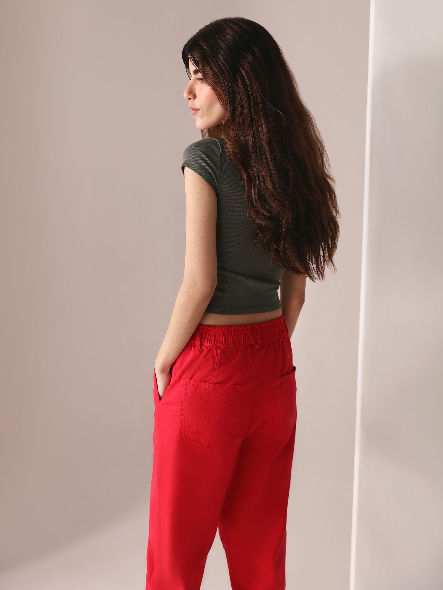 Woman wearing a grey top and casual wear red paper bag pants against a plain background