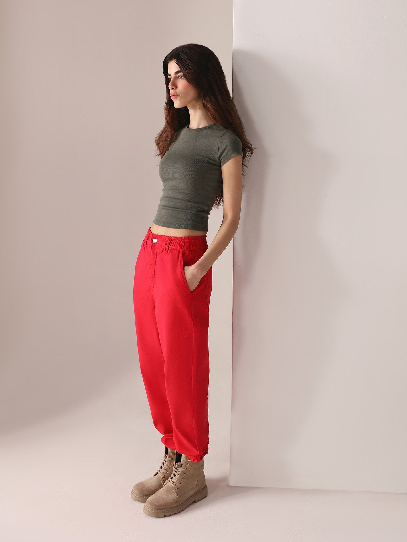 Woman wearing a grey top and casual wear red paper bag pants against a plain background